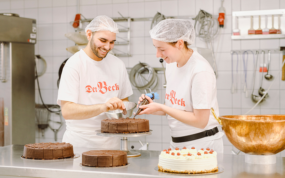 Zwei Konditoren von Der Beck verzieren eine Torte