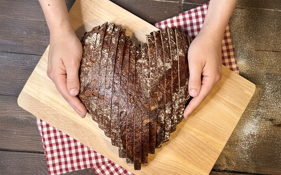 Hände halten in Herzform angeordnete Brotscheiben auf einem Holzbrett
