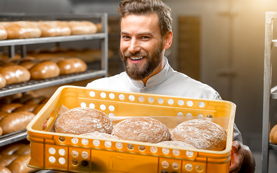 Bäckerei-Mitarbeiter steht mit einem Korb voller Brote vor einem Brotregal